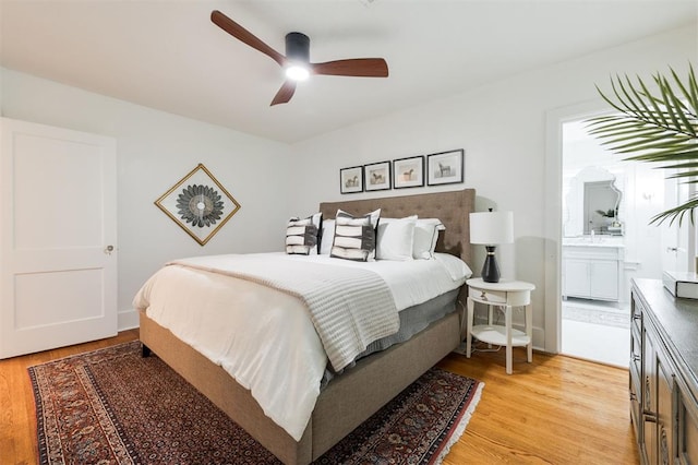 bedroom with light wood finished floors, ensuite bathroom, and a ceiling fan