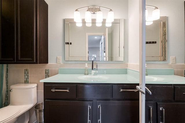 bathroom featuring toilet, vanity, and tile walls