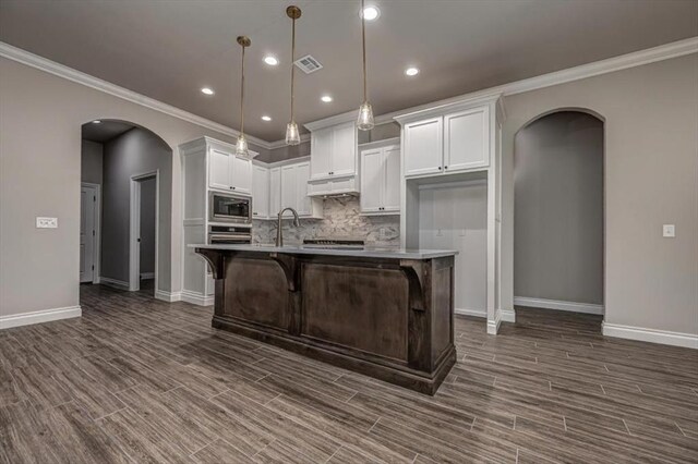 kitchen featuring built in microwave, arched walkways, stainless steel oven, baseboards, and crown molding