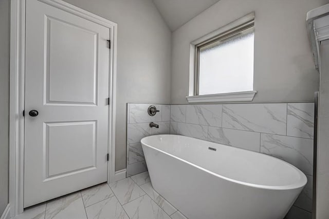 bathroom featuring marble look tile flooring, a soaking tub, tile walls, and vaulted ceiling