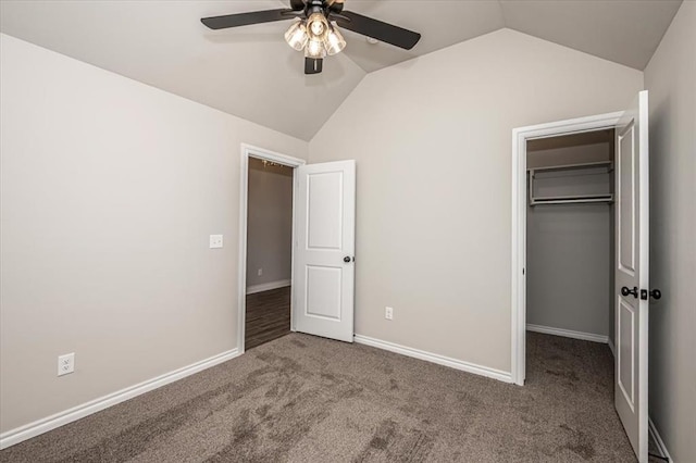 unfurnished bedroom featuring lofted ceiling, a spacious closet, carpet flooring, a closet, and a ceiling fan