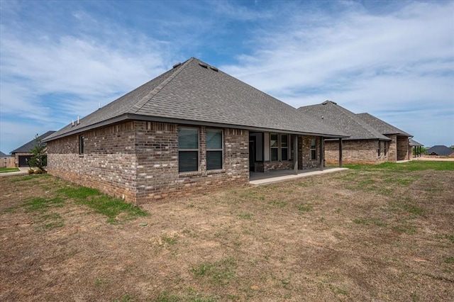 back of house featuring brick siding, a shingled roof, a patio area, and a lawn