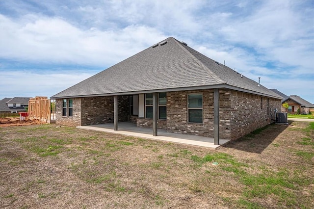 rear view of house with brick siding, central AC, a patio area, and roof with shingles