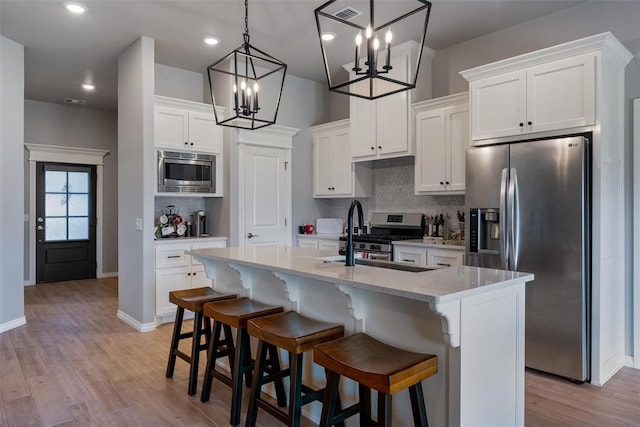 kitchen featuring stainless steel appliances, a chandelier, backsplash, white cabinetry, and a kitchen island with sink