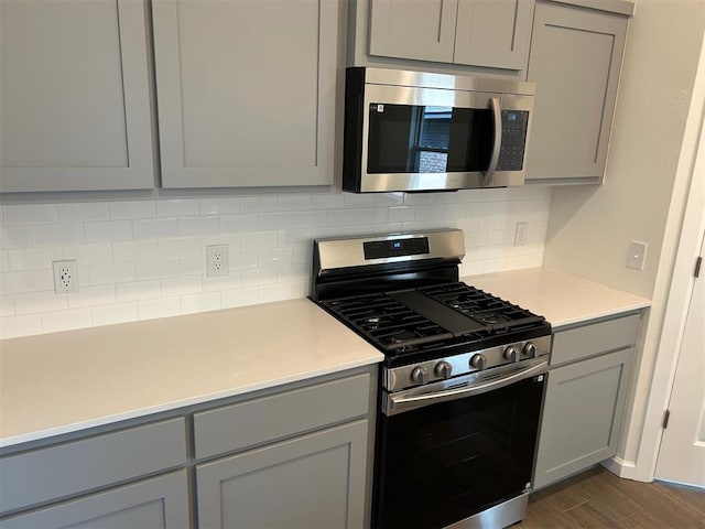 2933 NW 196th Pl, Edmond, OK 73012 - kitchen with appliances with stainless steel finishes, gray cabinetry, decorative backsplash, dark wood-type flooring, and light countertops