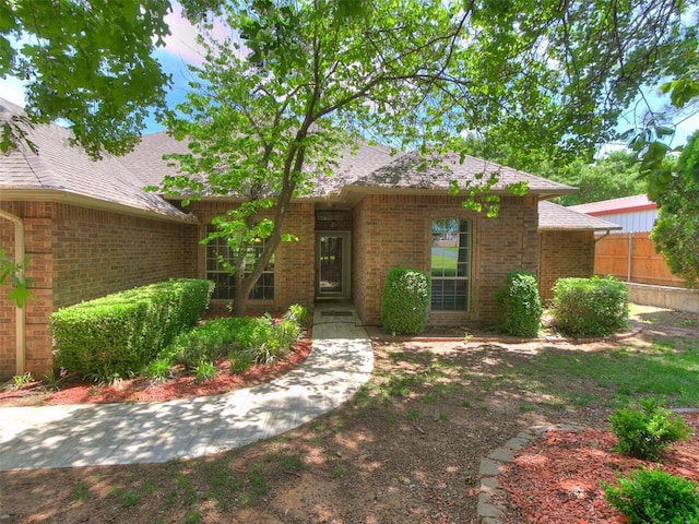 view of front of house with brick siding, fence, and roof with shingles