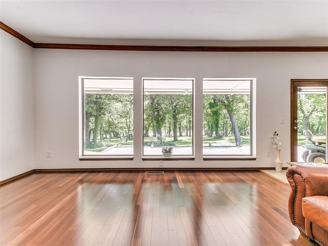 unfurnished living room with ornamental molding, wood finished floors, and baseboards