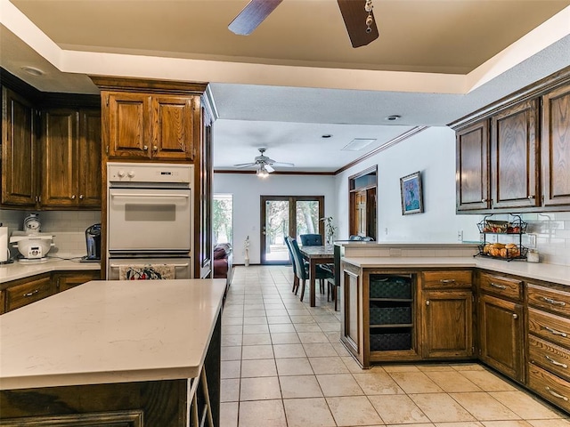 kitchen featuring a ceiling fan, light tile patterned floors, decorative backsplash, a peninsula, and ornamental molding