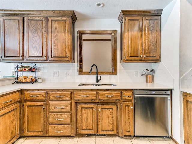 kitchen featuring stainless steel dishwasher, a sink, decorative backsplash, light countertops, and brown cabinets