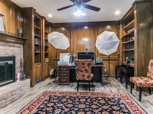 office area featuring a ceiling fan, light wood-style floors, a fireplace, and wood walls
