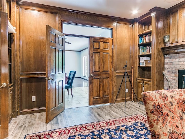 office area featuring light wood-type flooring, crown molding, wooden walls, a brick fireplace, and baseboards