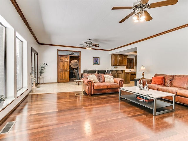 living area featuring a ceiling fan, ornamental molding, light wood finished floors, and baseboards