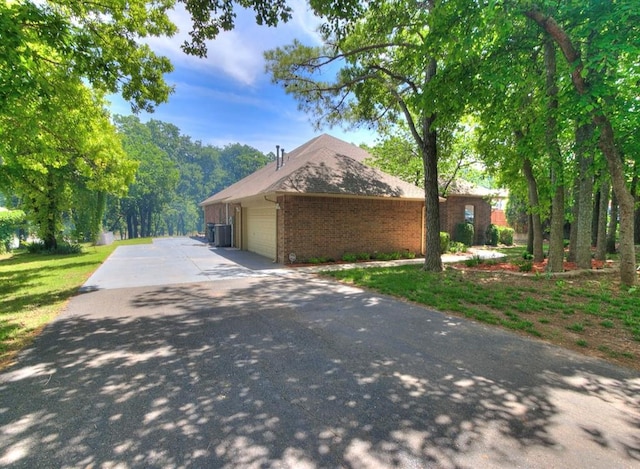 view of side of home with an attached garage, driveway, and brick siding