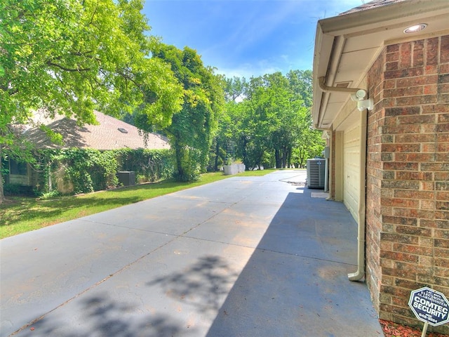 view of side of property featuring central AC unit, brick siding, and a garage
