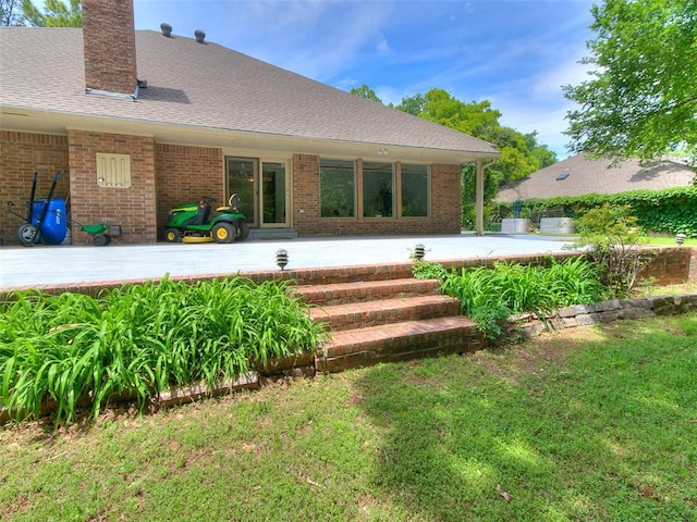 rear view of house with a patio, brick siding, a chimney, and a lawn