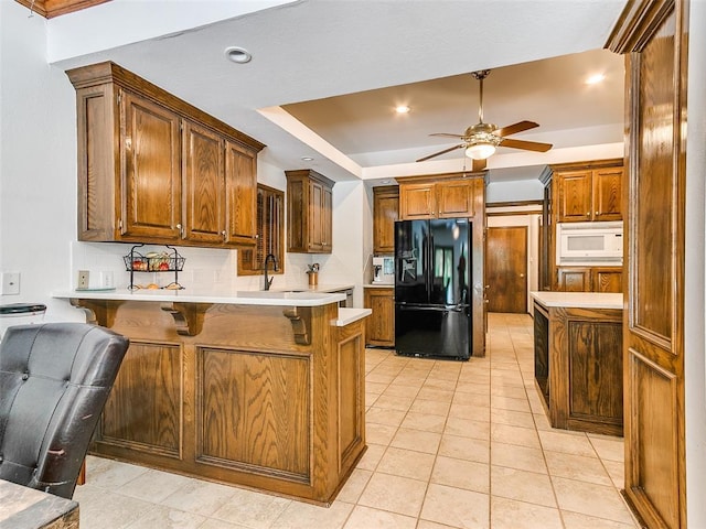 kitchen featuring black fridge with ice dispenser, white microwave, a peninsula, a ceiling fan, and a breakfast bar