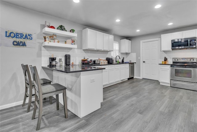 kitchen featuring appliances with stainless steel finishes, backsplash, dark countertops, recessed lighting, and a breakfast bar area