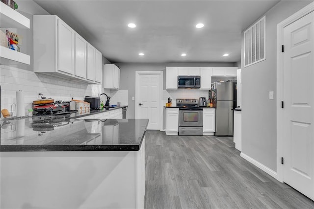 kitchen featuring stainless steel appliances, dark stone countertops, a peninsula, backsplash, and light wood finished floors