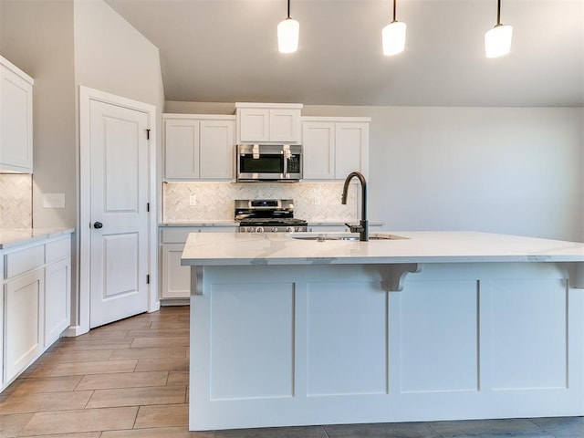 8617 NW 77th St, Oklahoma City, OK 73132 - kitchen featuring appliances with stainless steel finishes, a sink, tasteful backsplash, white cabinets, and a center island with sink