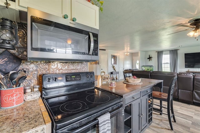 2316 E 68th St, Stillwater, OK 74074 - kitchen featuring black electric range, stainless steel microwave, open floor plan, ceiling fan, and light wood-style flooring