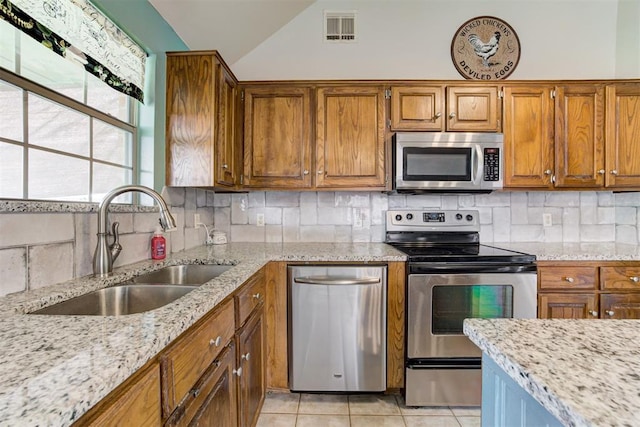 1312 SW 25th St, Moore, OK 73170 - kitchen featuring appliances with stainless steel finishes, a sink, brown cabinetry, light stone counters, and light tile patterned flooring