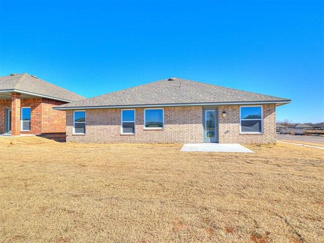 1121 Acacia Creek Dr, Yukon, OK 73099 - back of house featuring a patio, brick siding, roof with shingles, and a lawn