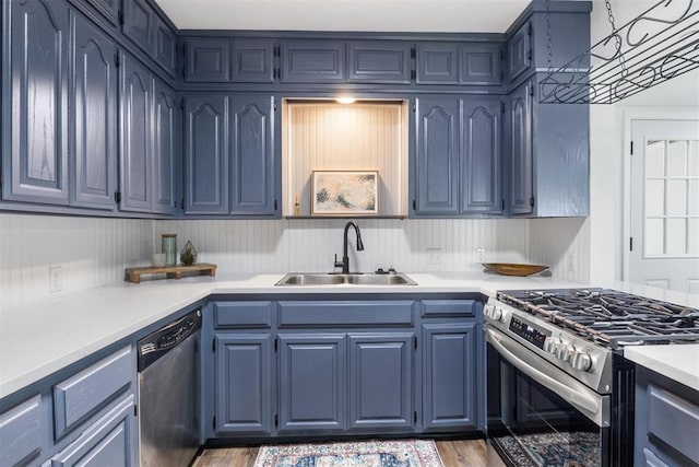 kitchen with stainless steel appliances, a sink, wood finished floors, light countertops, and blue cabinets
