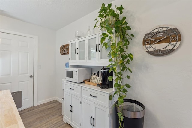 711 Spruce Dr, Yukon, OK 73099 - kitchen with white microwave, light countertops, light wood-type flooring, white cabinets, and glass insert cabinets