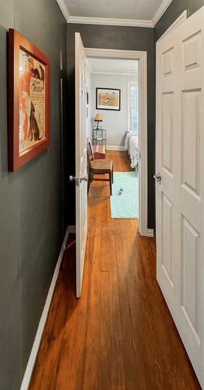 hall featuring wood finished floors, baseboards, and crown molding