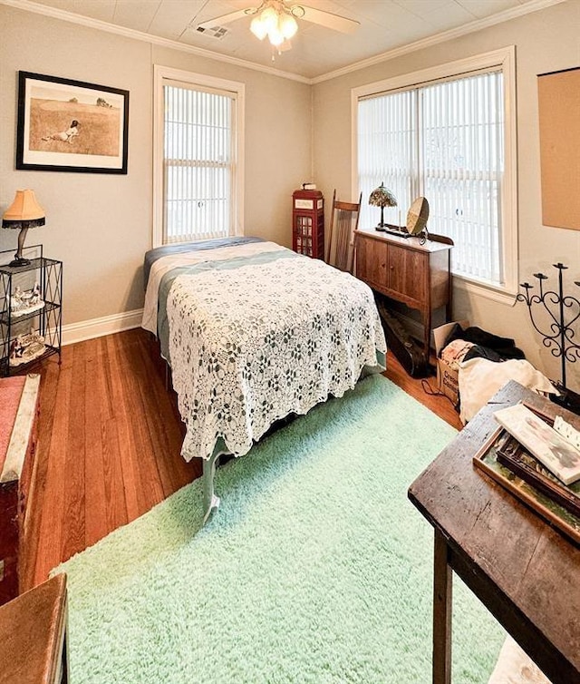 bedroom with wood finished floors, ornamental molding, baseboards, multiple windows, and a ceiling fan