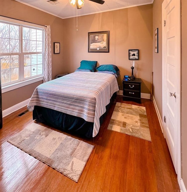 bedroom with ornamental molding, wood finished floors, and baseboards