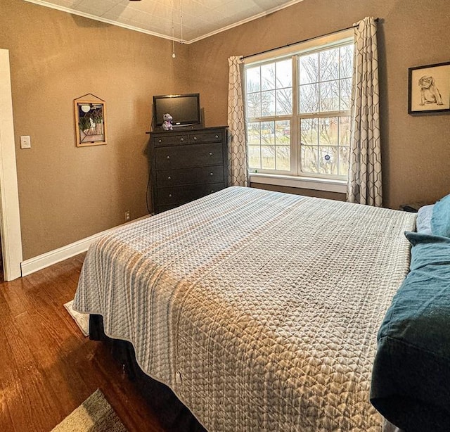 bedroom featuring wood finished floors, ornamental molding, baseboards, and a textured wall