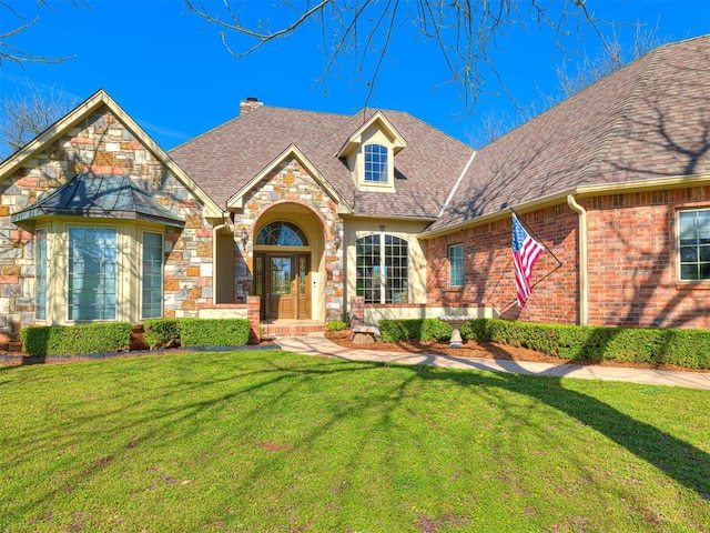 view of front of house featuring a chimney, a front lawn, stone siding, and a shingled roof