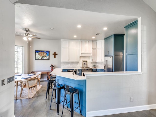 kitchen featuring high end refrigerator, wood finished floors, a ceiling fan, recessed lighting, and a kitchen breakfast bar