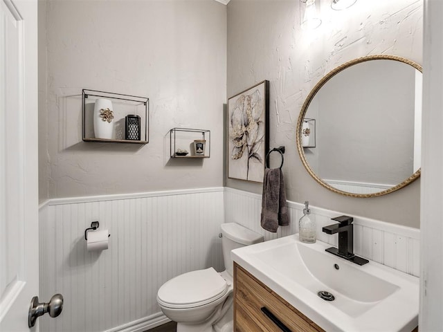 half bath with wainscoting, toilet, and vanity