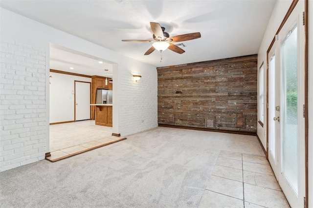 empty room featuring ceiling fan, light colored carpet, wooden walls, and brick wall
