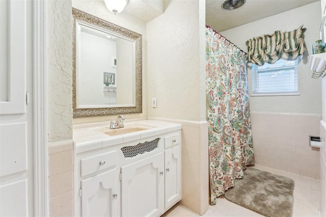 full bathroom with a wainscoted wall, tile walls, tile patterned floors, vanity, and curtained shower