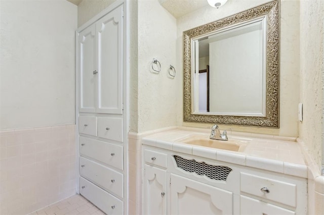 bathroom featuring vanity, wainscoting, and a textured wall
