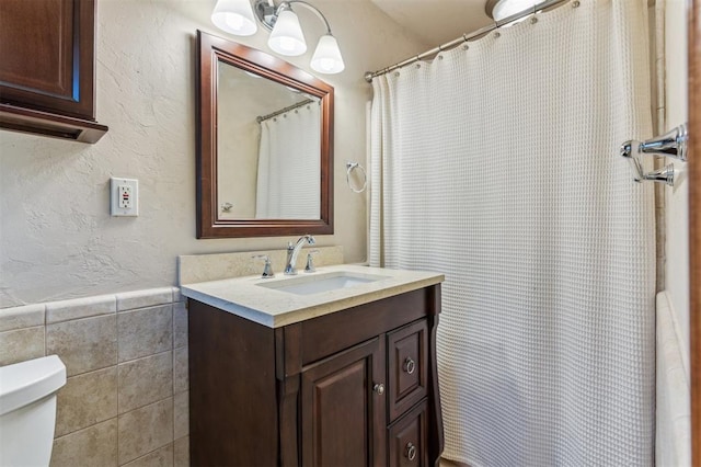 bathroom featuring tile walls, toilet, vanity, wainscoting, and a textured wall