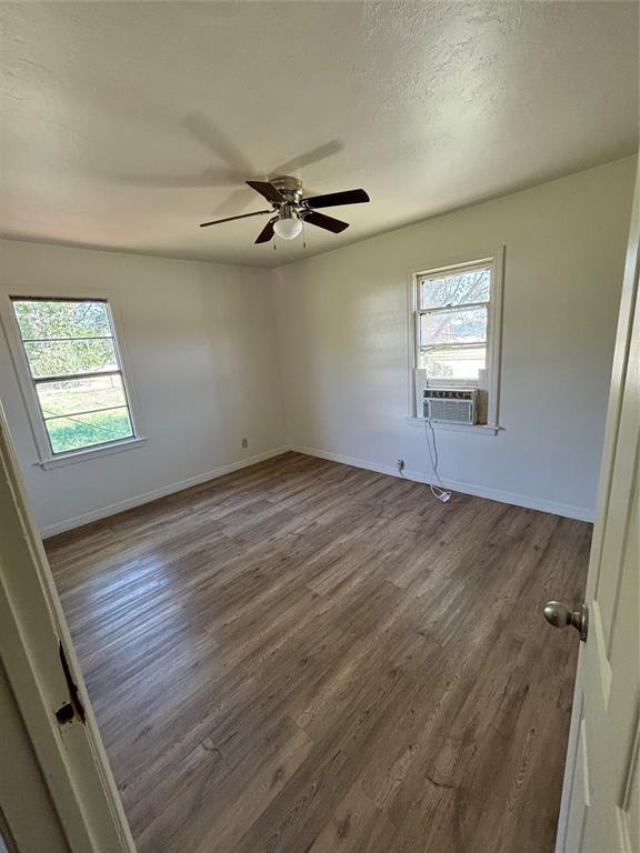 1011 E Sutherland St, Altus, OK 73521 - spare room featuring healthy amount of natural light, dark wood-type flooring, baseboards, and cooling unit