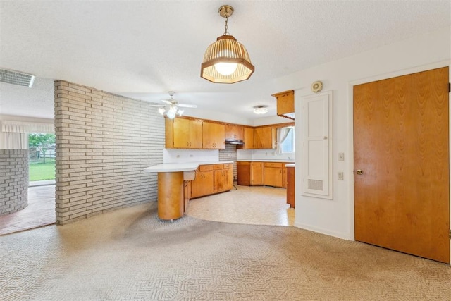 1009 Cherokee Pl, Lindsay, OK 73052 - kitchen featuring light countertops, brown cabinets, light carpet, a peninsula, and brick wall