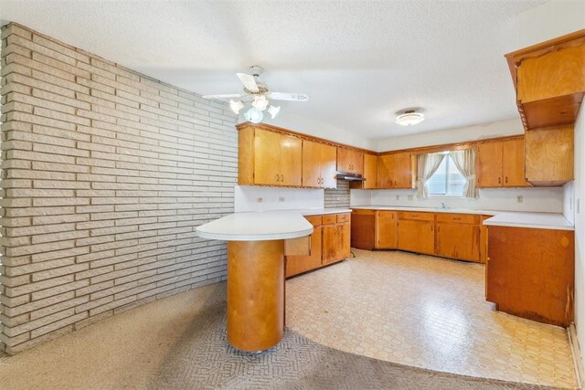 1009 Cherokee Pl, Lindsay, OK 73052 - kitchen featuring a peninsula, a textured ceiling, brick wall, brown cabinets, and light countertops
