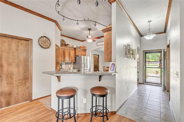 8701 Long Spur Trl, Edmond, OK 73034 - kitchen with stainless steel refrigerator with ice dispenser, crown molding, a breakfast bar, baseboards, and brown cabinetry