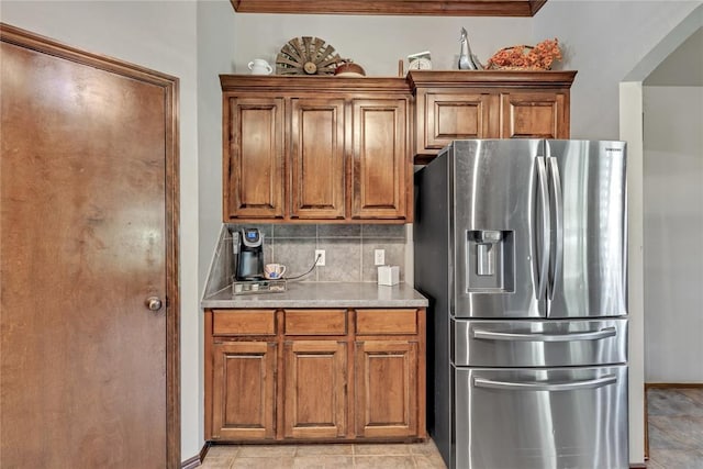8701 Long Spur Trl, Edmond, OK 73034 - kitchen featuring stainless steel fridge with ice dispenser, brown cabinets, decorative backsplash, light countertops, and crown molding