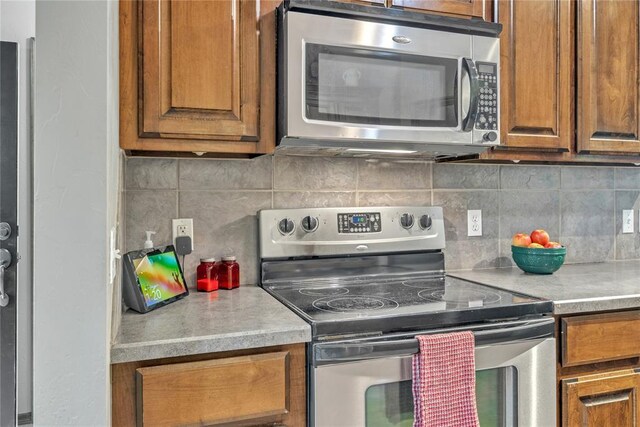 8701 Long Spur Trl, Edmond, OK 73034 - kitchen featuring appliances with stainless steel finishes, brown cabinetry, and decorative backsplash