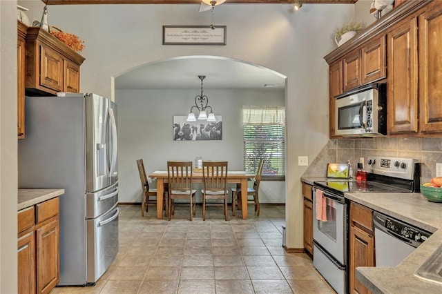 8701 Long Spur Trl, Edmond, OK 73034 - kitchen with stainless steel appliances, arched walkways, brown cabinets, tasteful backsplash, and light countertops
