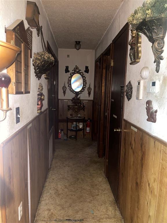 811 N Admire Ave, El Reno, OK 73036 - corridor with a textured ceiling, wainscoting, light colored carpet, and wooden walls