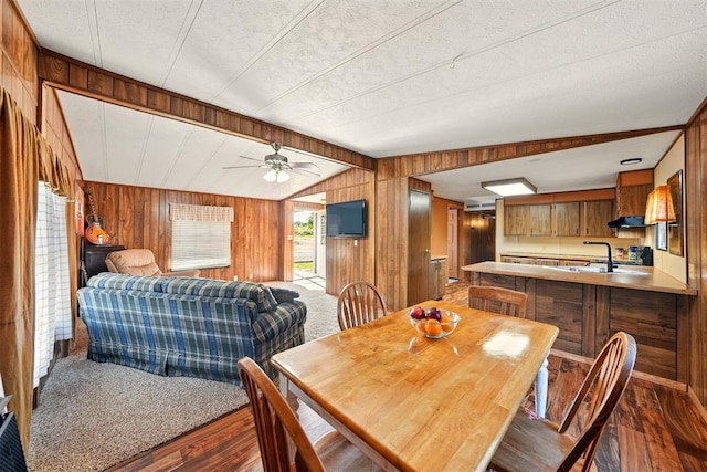 dining space featuring wood walls, dark wood-style floors, a ceiling fan, and lofted ceiling