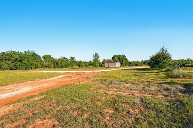 view of green lawn with dirt driveway, a rural view, and a garage