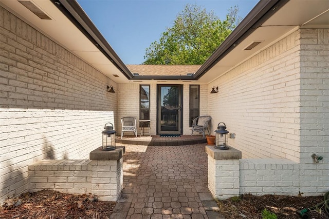 entrance to property featuring brick siding, a patio area, and a shingled roof